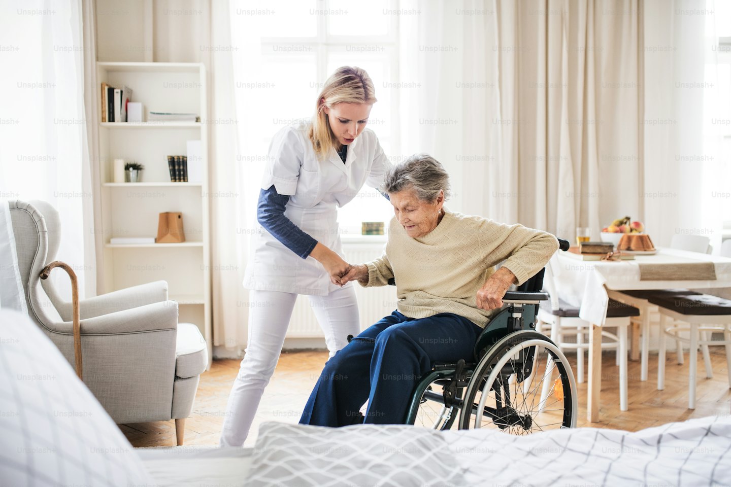 Caregiver in uniform helps a woman stand from her wheelchair.